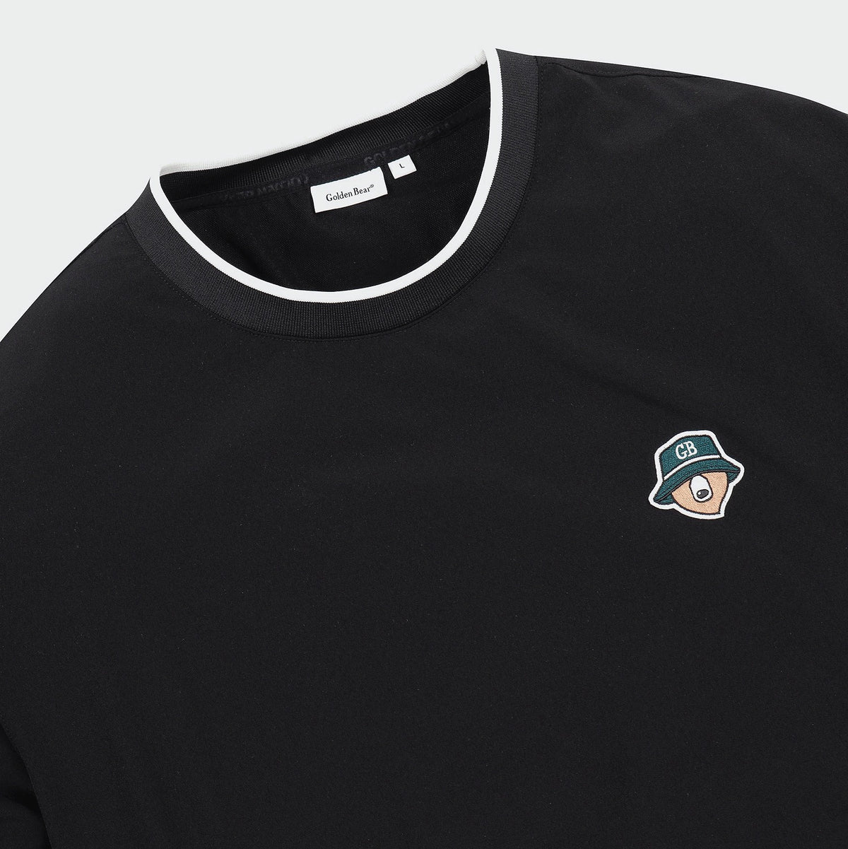 Close-up of a black crewneck t-shirt with a white contrast trim along the collar and a small embroidered cartoon character on the left chest. The brand label inside the collar reads 'Golden Bear'.
