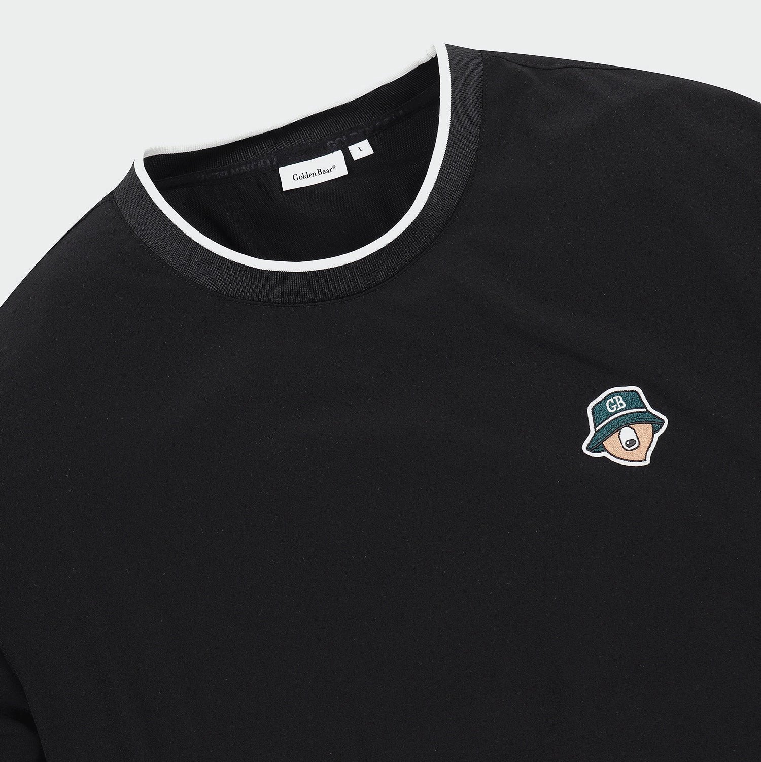 Close-up of a black crewneck t-shirt with a white contrast trim along the collar and a small embroidered cartoon character on the left chest. The brand label inside the collar reads 'Golden Bear'.