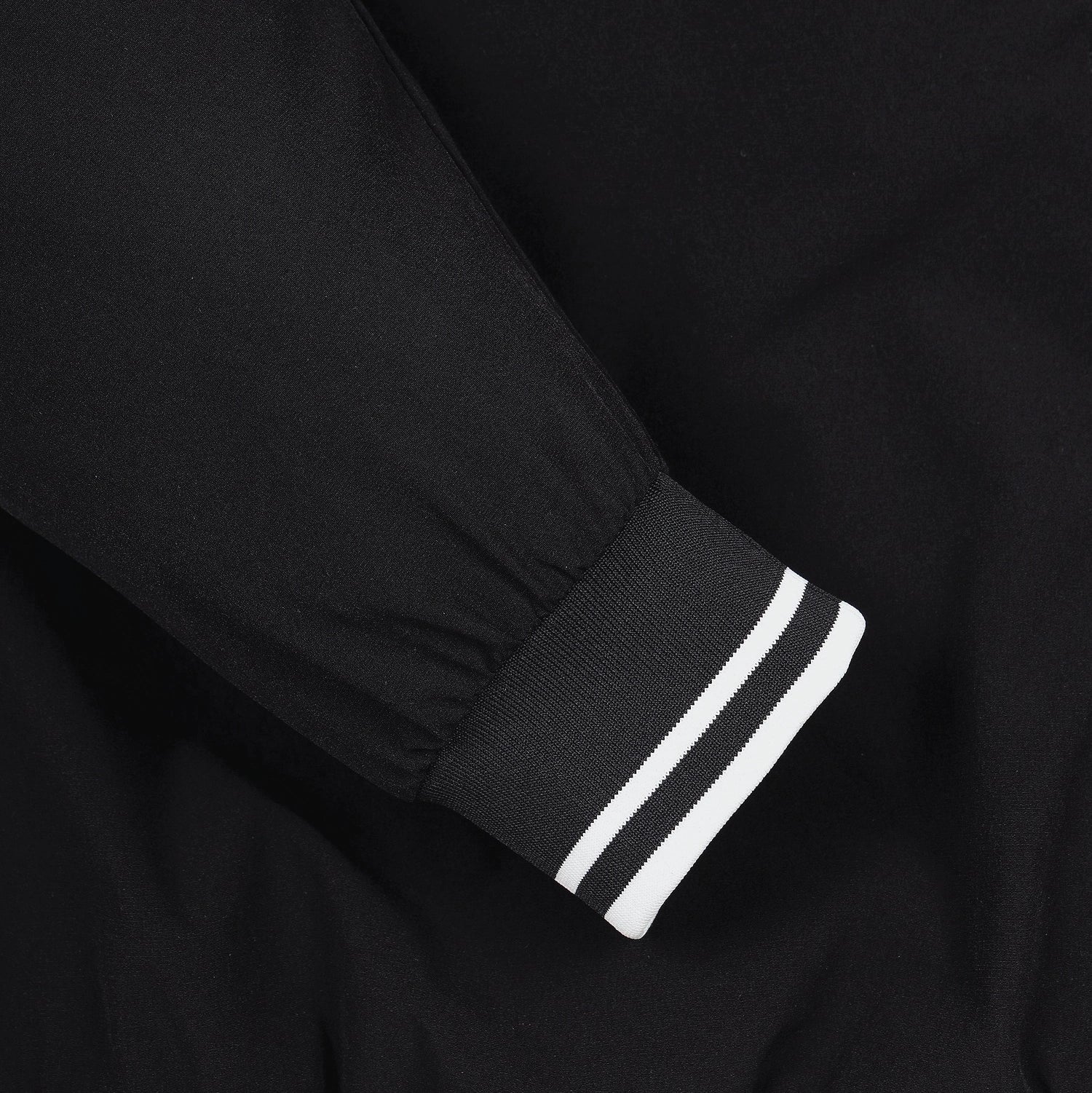 Close-up of a black sleeve with a ribbed cuff featuring two white stripes.