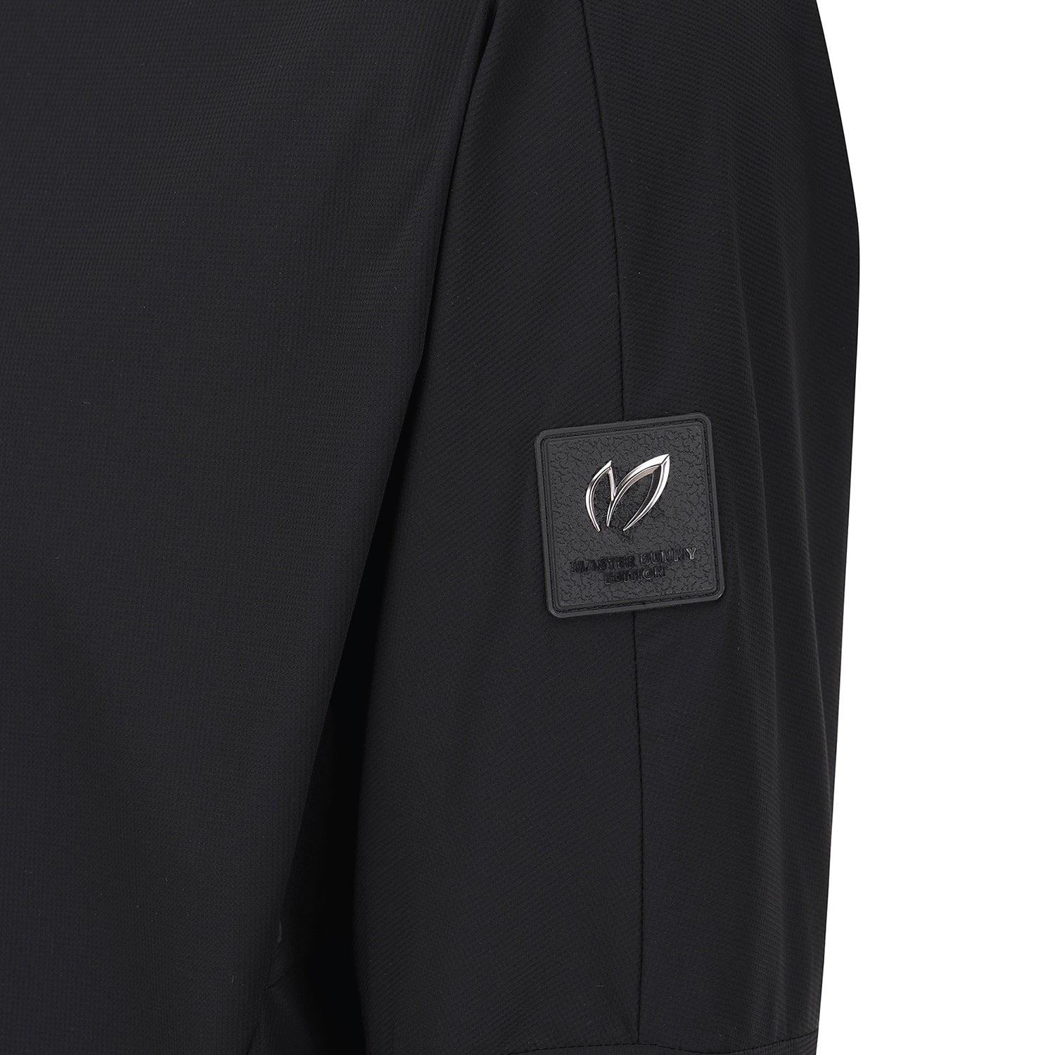 Close-up of a black textured garment sleeve featuring a square black brand patch with a silver-toned leaf logo and the text 'MASTER BUNNY EDITION' on the upper arm.
