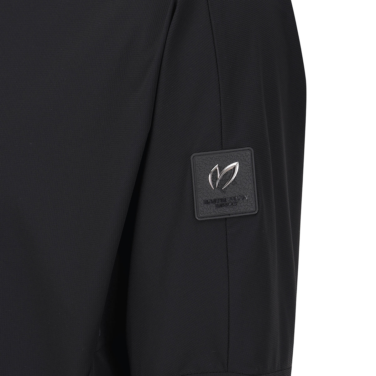 Close-up of a black textured garment sleeve featuring a square black brand patch with a silver-toned leaf logo and the text 'MASTER BUNNY EDITION' on the upper arm.