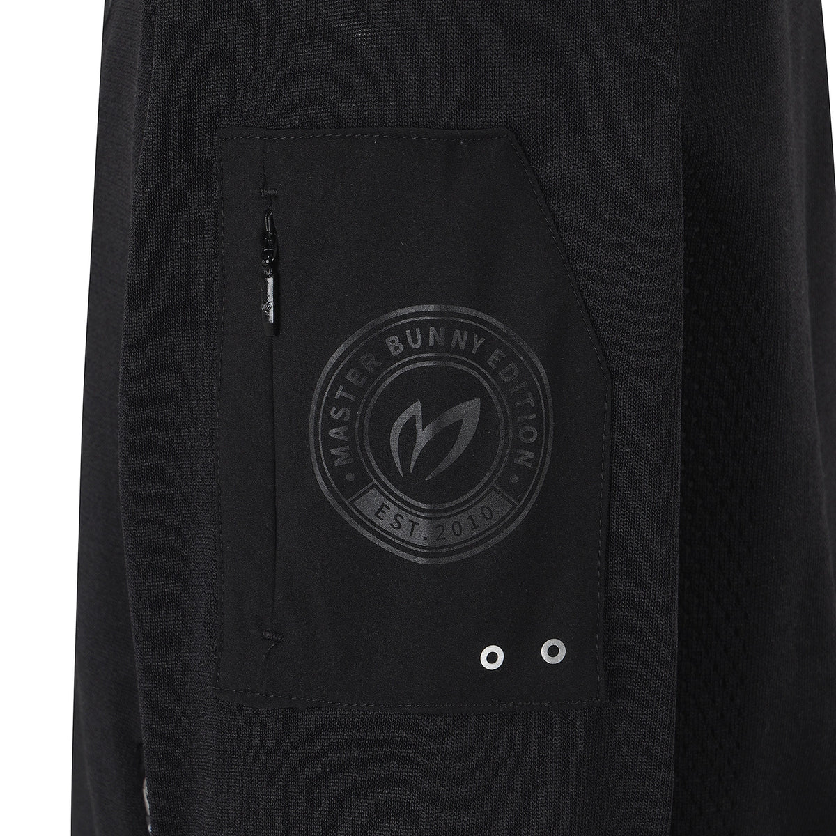 Close-up of a black textured garment, likely a jacket or hoodie, featuring a front pocket with a tonal circular 'Master Bunny Edition' logo and silver grommets.
