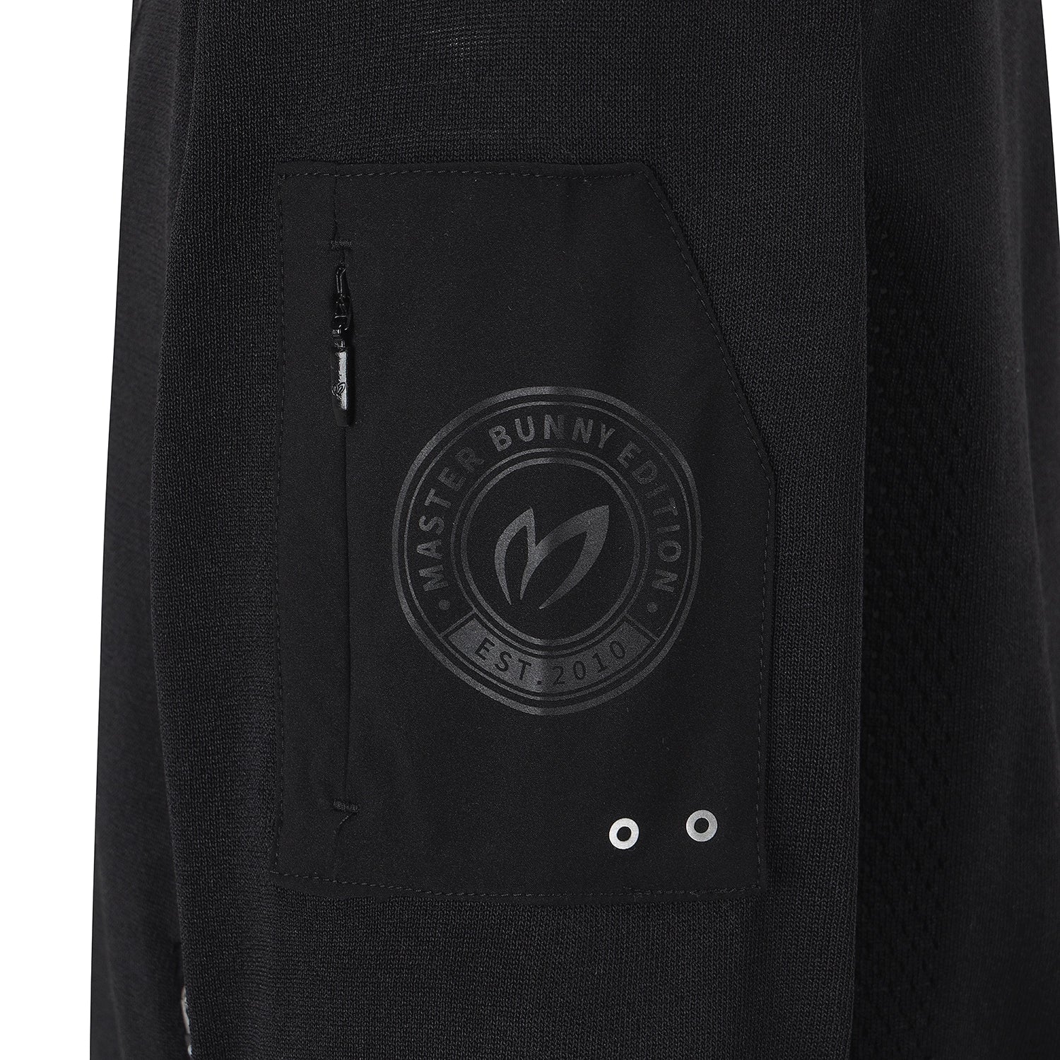 Close-up of a black textured garment, likely a jacket or hoodie, featuring a front pocket with a tonal circular 'Master Bunny Edition' logo and silver grommets.