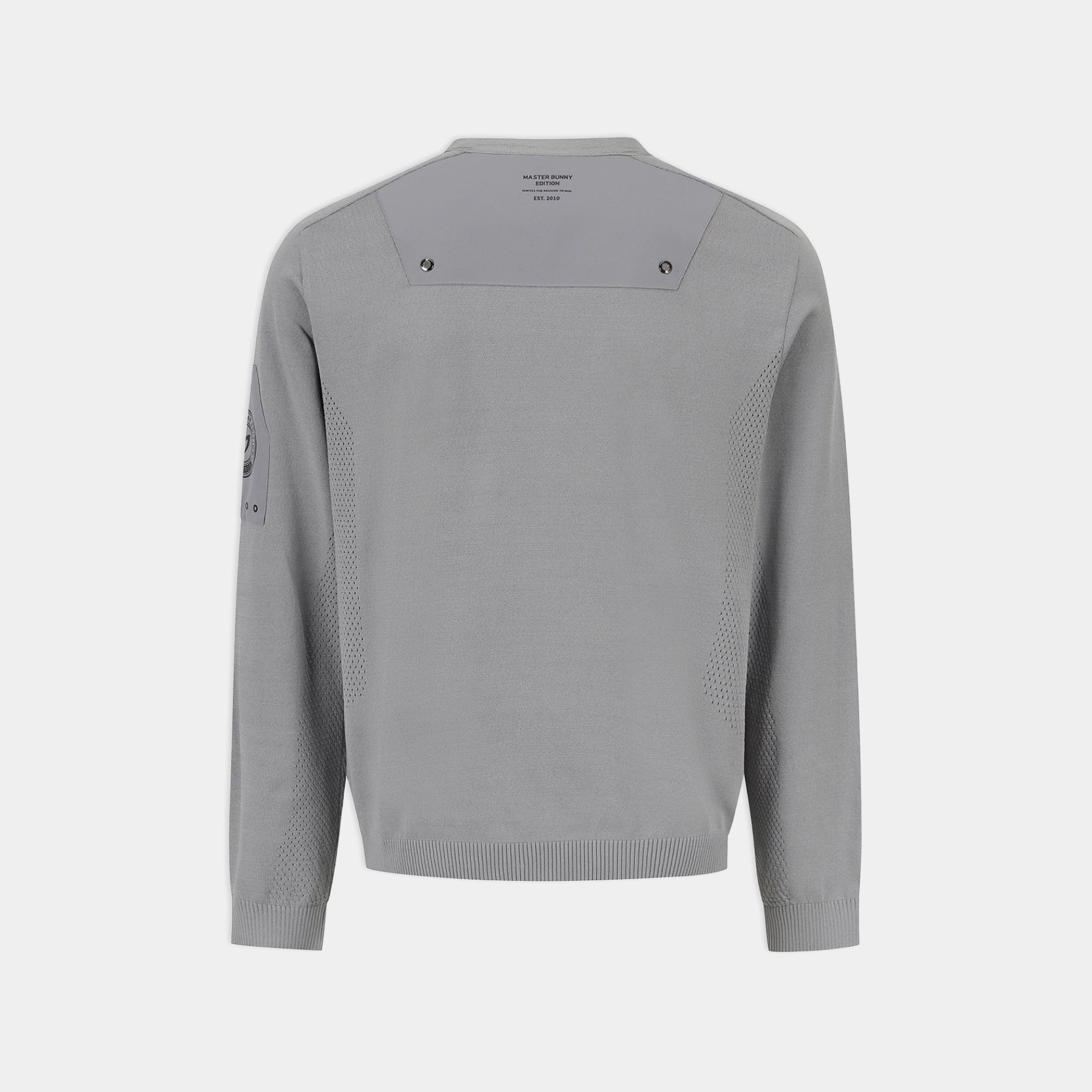 A light gray knit sweater shown from the back, featuring a wide shoulder yoke with small dark logo details, textured knit side panels, and a small dark graphic on the left sleeve, set against a solid light gray background.