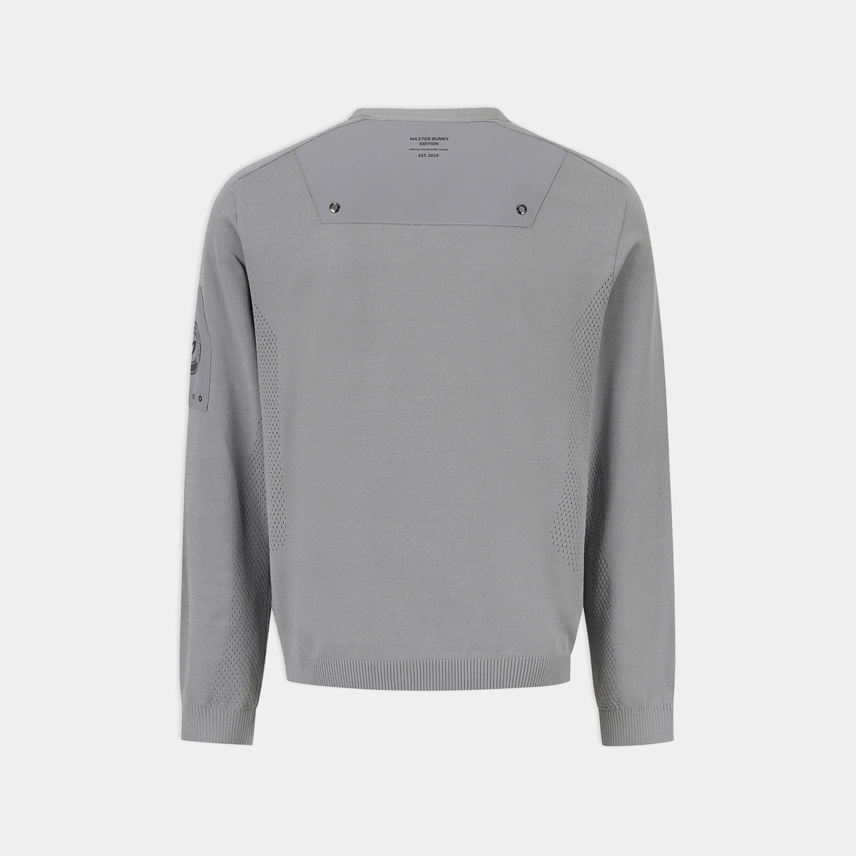 A light gray knit sweater shown from the back, featuring a wide shoulder yoke with small dark logo details, textured knit side panels, and a small dark graphic on the left sleeve, set against a solid light gray background.