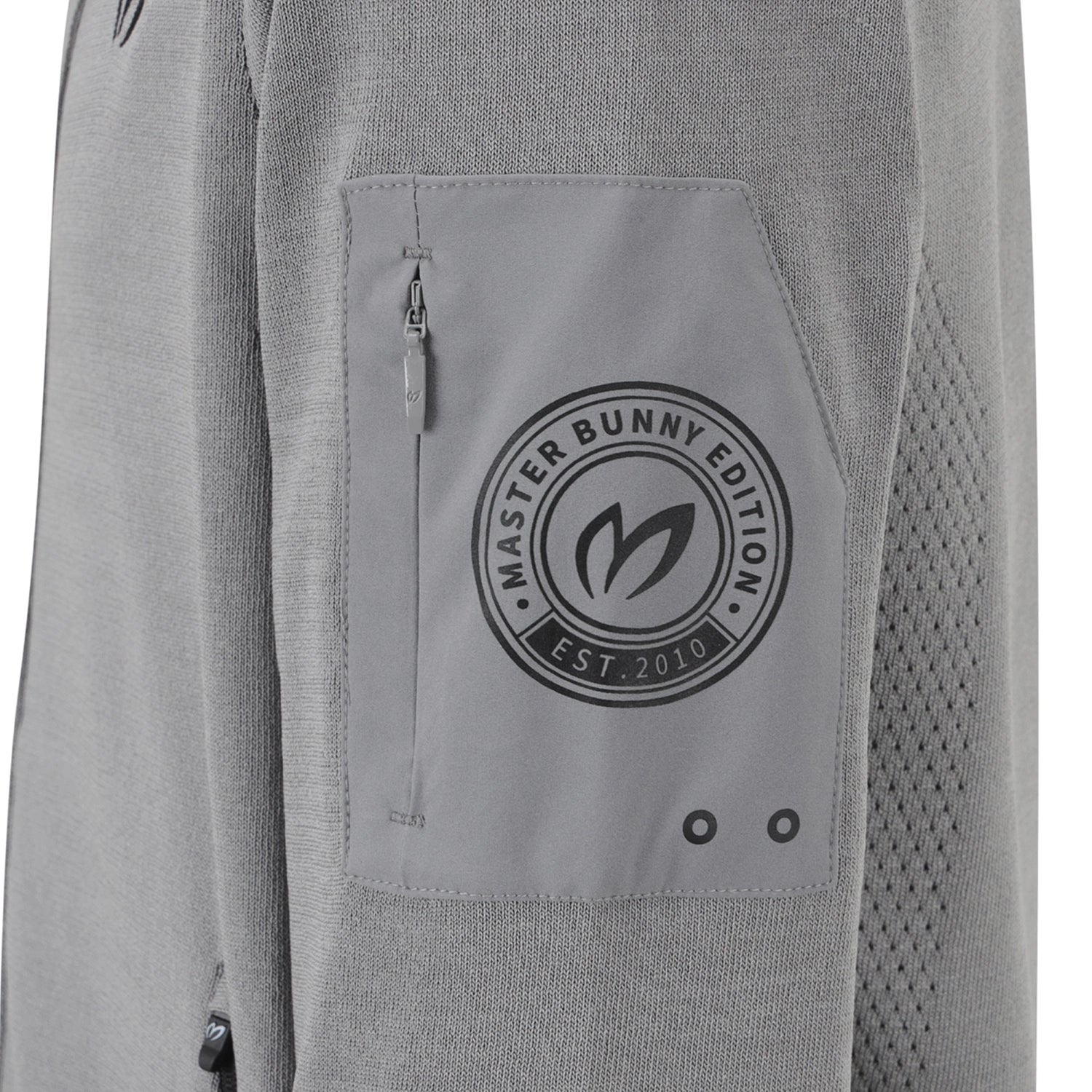 Close-up of a light gray knit jacket featuring a zippered pocket with a circular black 'Master Bunny Edition' logo patch.