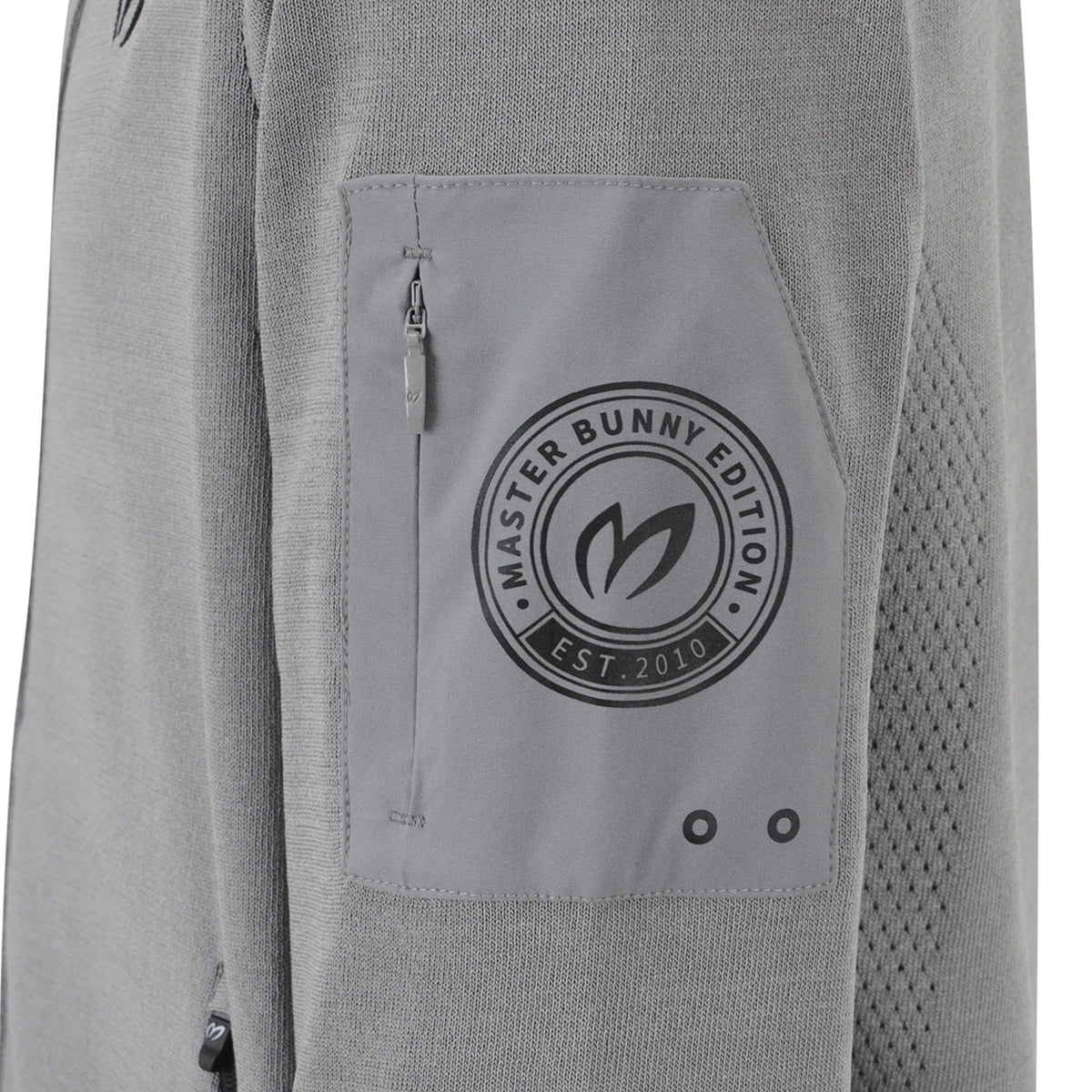 Close-up of a light gray knit jacket featuring a zippered pocket with a circular black 'Master Bunny Edition' logo patch.