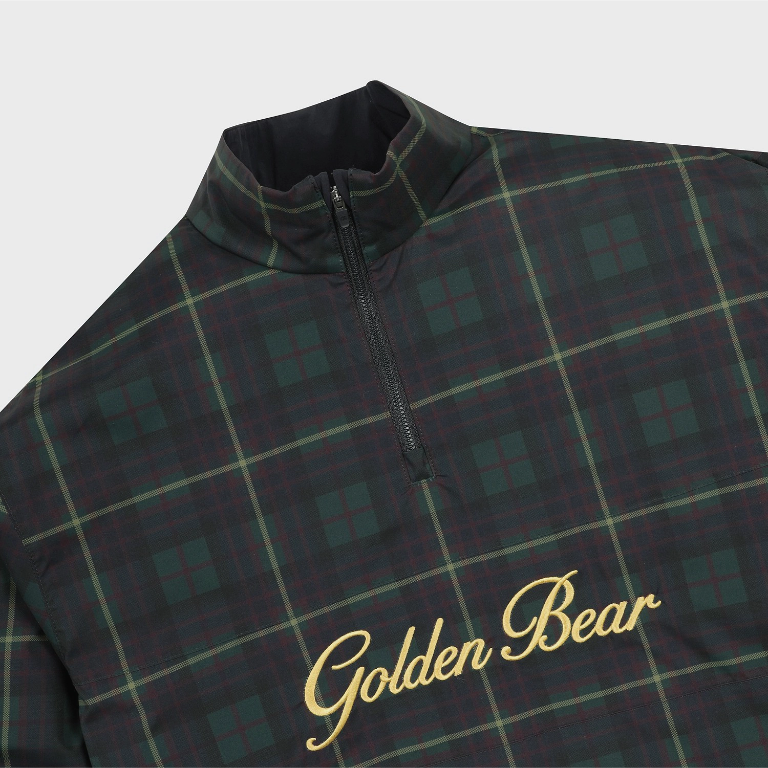 A close-up of a Golden Bear quarter-zip pullover featuring a dark green and black tartan plaid pattern with gold embroidered script on the chest.