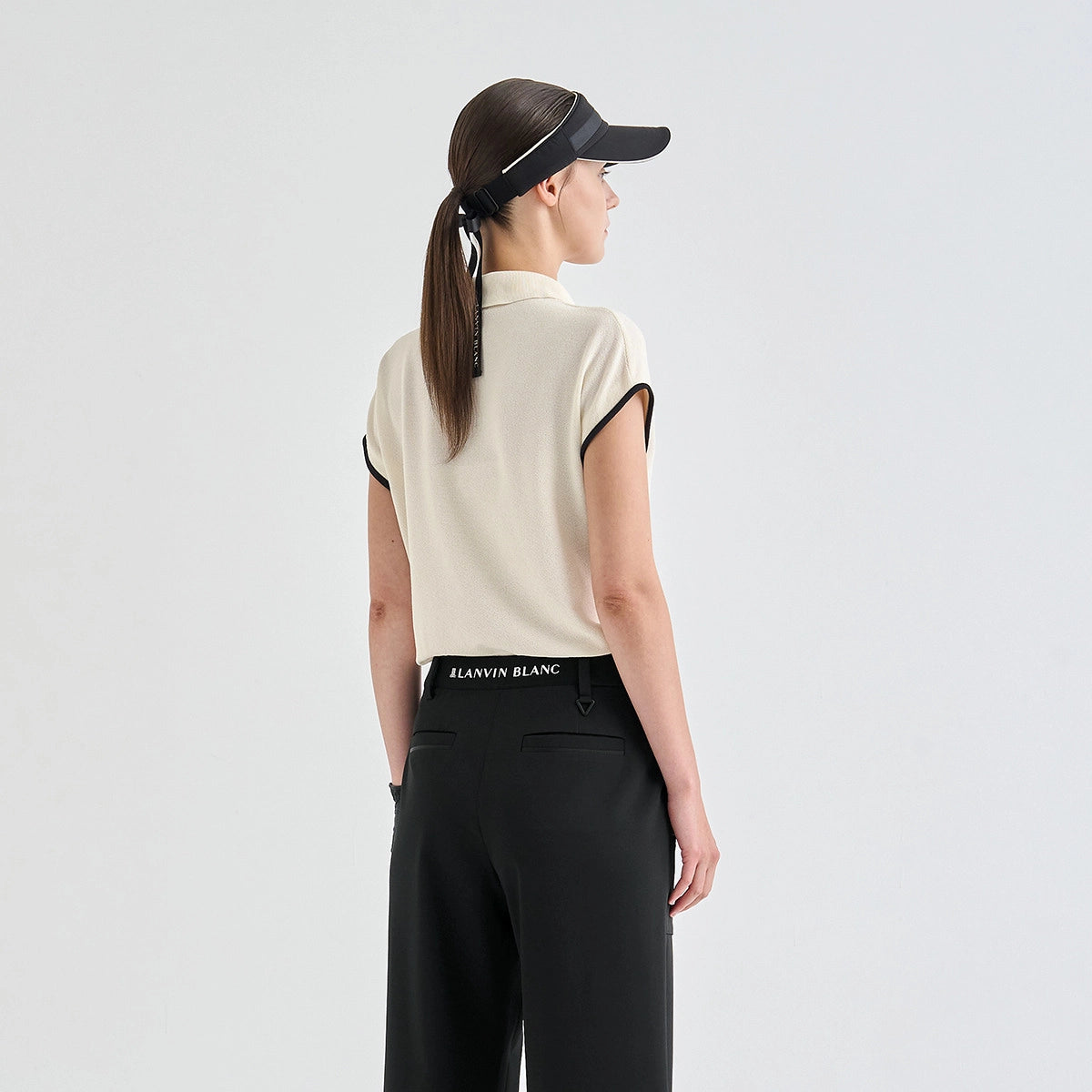 A woman shown from the back wearing a cream short-sleeve knit top with black trim, black pants, and a black visor. The waistband of the top shows the brand name 'LANVIN BLANC'.