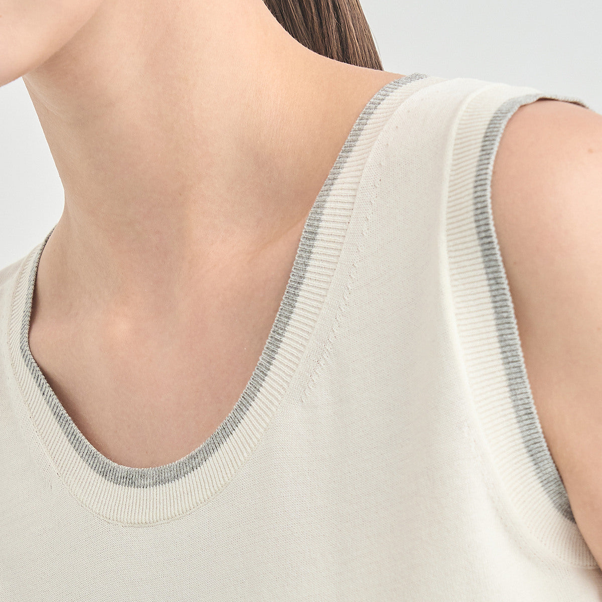 Close-up of a model wearing a light beige ribbed knit tank top with a contrasting gray ribbed trim around the scoop neckline.