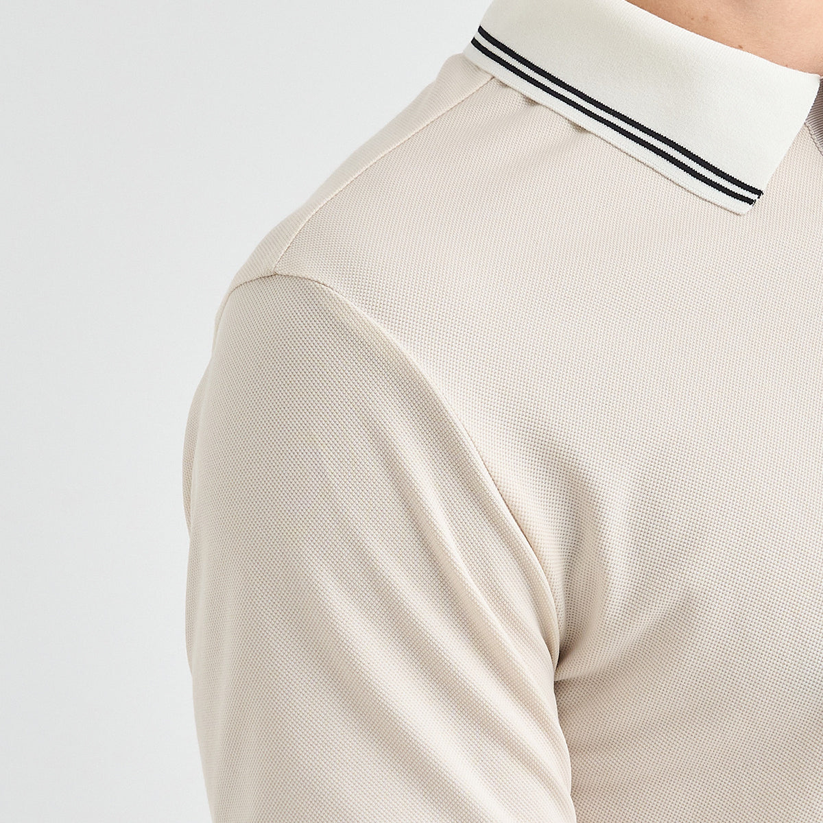 Close-up of a person wearing a light beige textured polo shirt with a white collar featuring two thin black stripes.