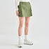 A model wearing an olive green cargo-style mini skirt with flap pockets, paired with white socks and white sneakers, shown from the waist down on a light gray studio background.
