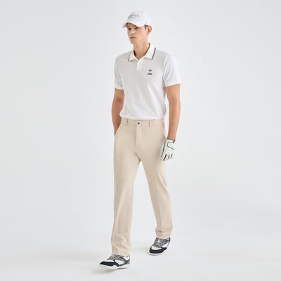 A man modeling a white short-sleeve polo shirt with dark piping, beige golf pants, a white cap, and a golf glove against a light gray studio background.