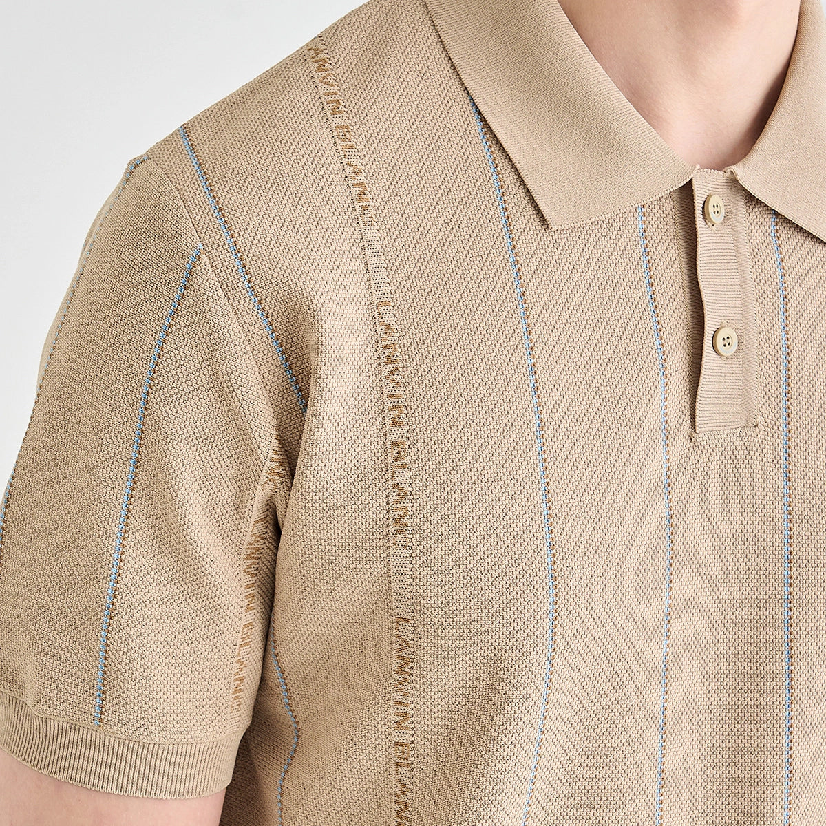 Close-up of a beige knit polo shirt with thin vertical blue stripes and a repeating text detail running down the center front, worn by a model.