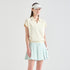 A woman modeling a light cream short-sleeve polo shirt and a light mint green pleated tennis skirt against a plain light gray studio background.