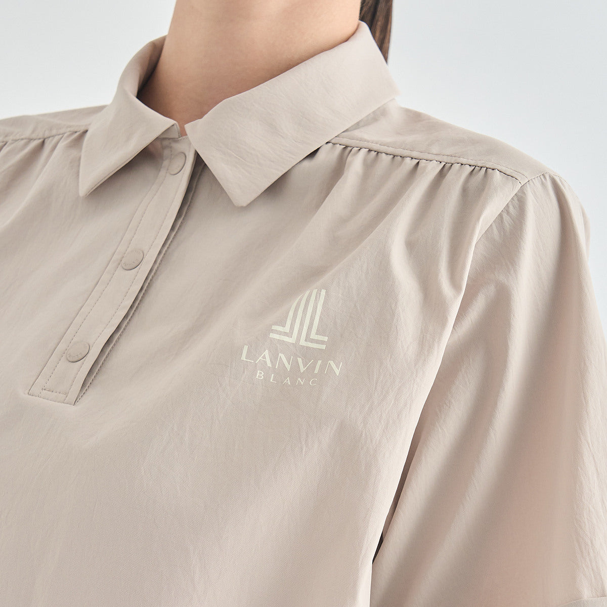 Close-up of a person wearing a light beige Lanvin Blanc collared button-front top with a subtle tonal logo on the chest.