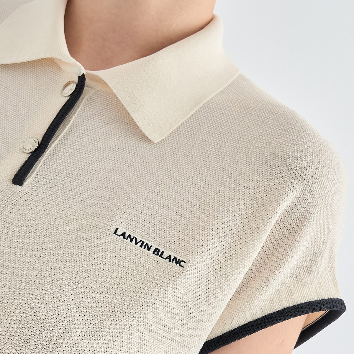 Close-up of a person wearing a short-sleeve polo shirt in off-white/cream with black trim and the words 'LANVIN BLANC' embroidered on the chest.