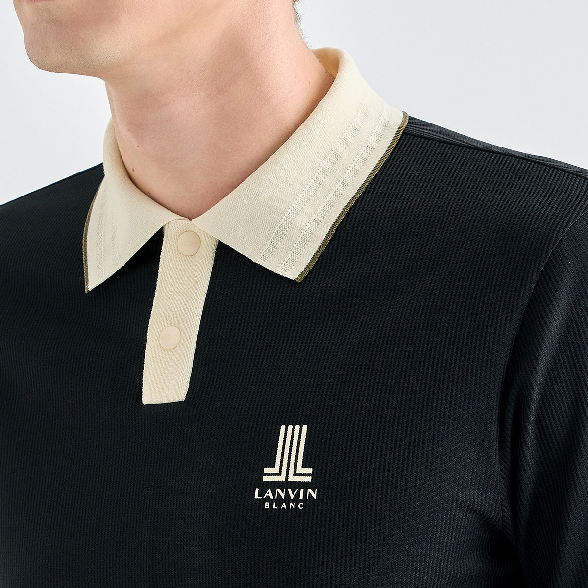Close-up of a person wearing a black ribbed polo shirt with a contrasting cream collar and placket, featuring the LANVIN BLANC logo on the chest.