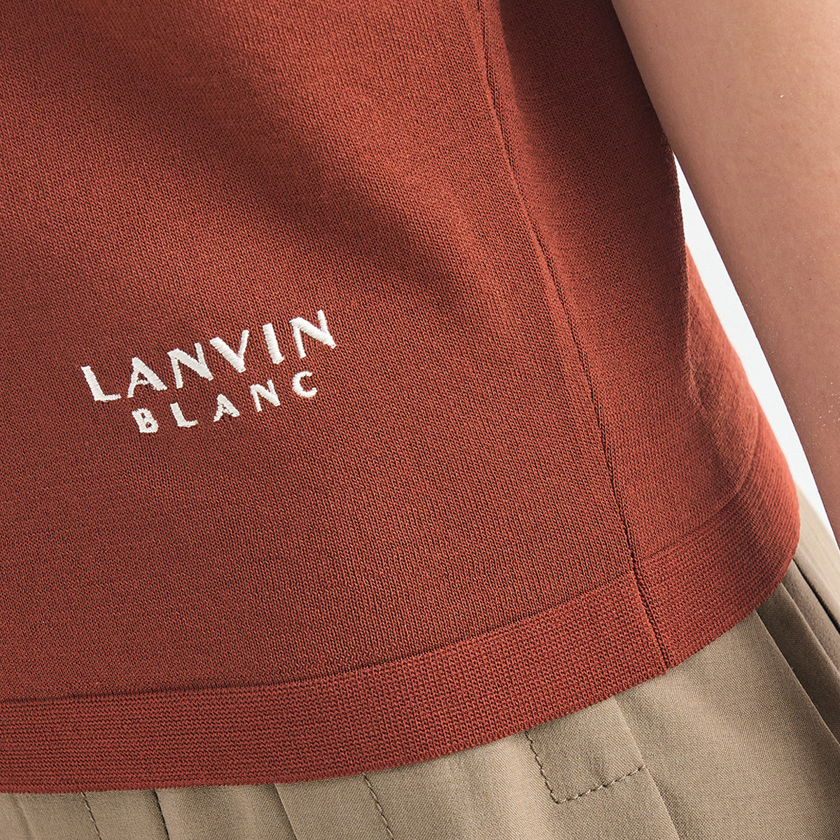 Close-up of a terracotta-colored knit top with white embroidered 'LANVIN BLANC' branding on the chest, worn with beige trousers.