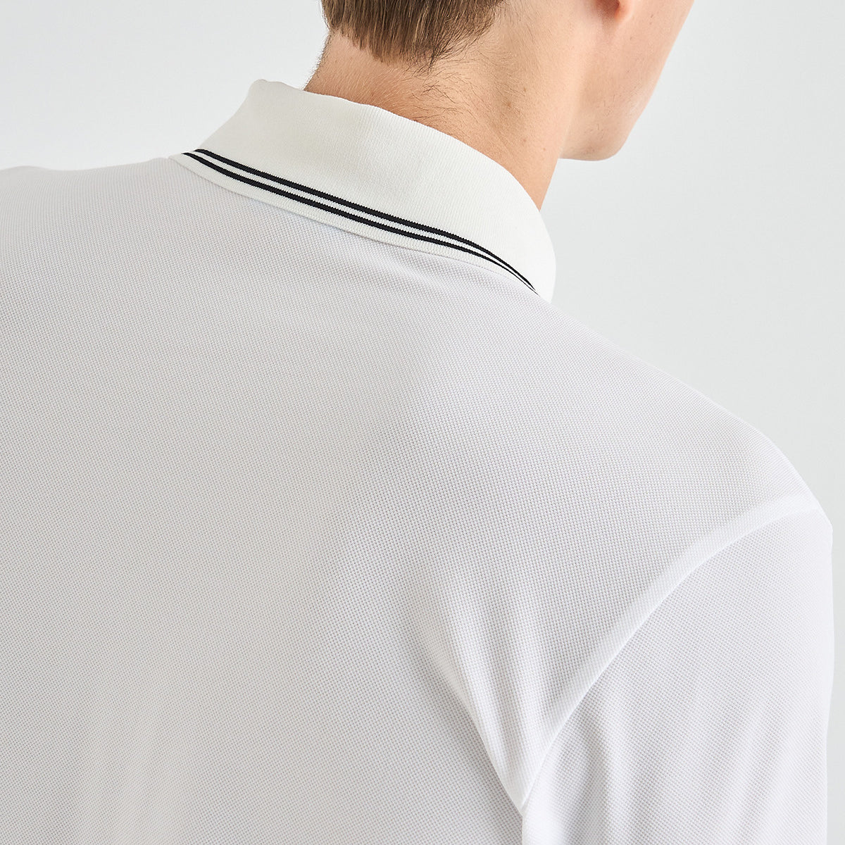 Close-up back view of a man wearing a white polo shirt with a black double stripe accent on the collar, against a light gray background.