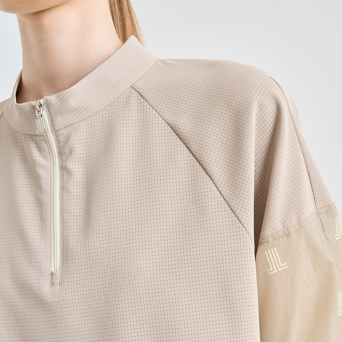 Close-up of a model wearing a light beige athletic quarter-zip pullover with a fine mesh texture and tonal embroidered sleeve details.