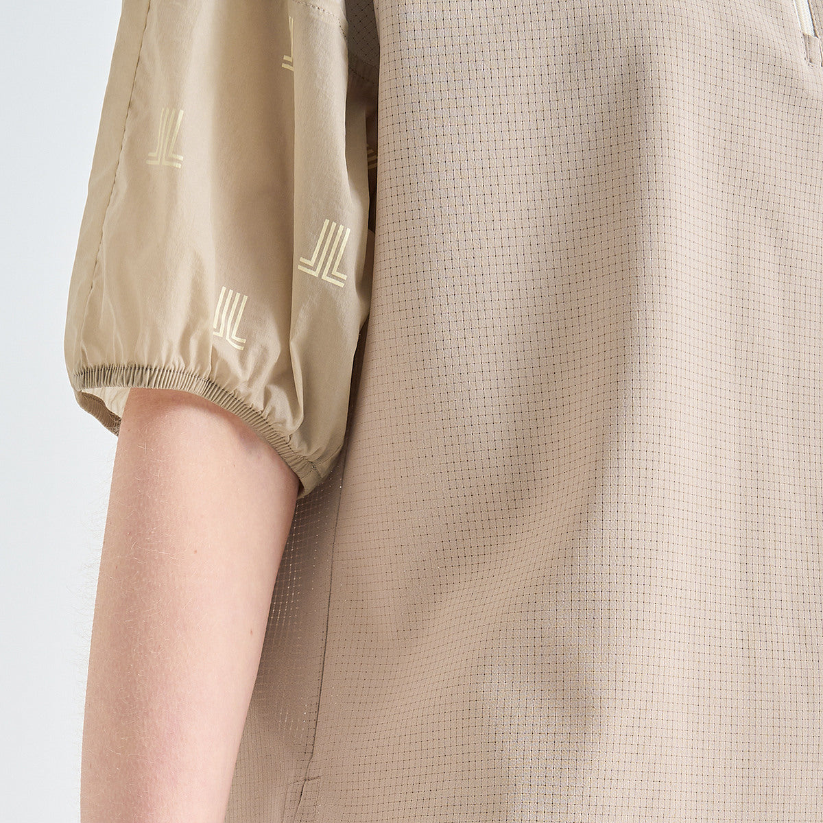 Close-up of a beige short-sleeve top with a fine mesh texture and tonal embroidered geometric logos on the sleeve, worn by a model.