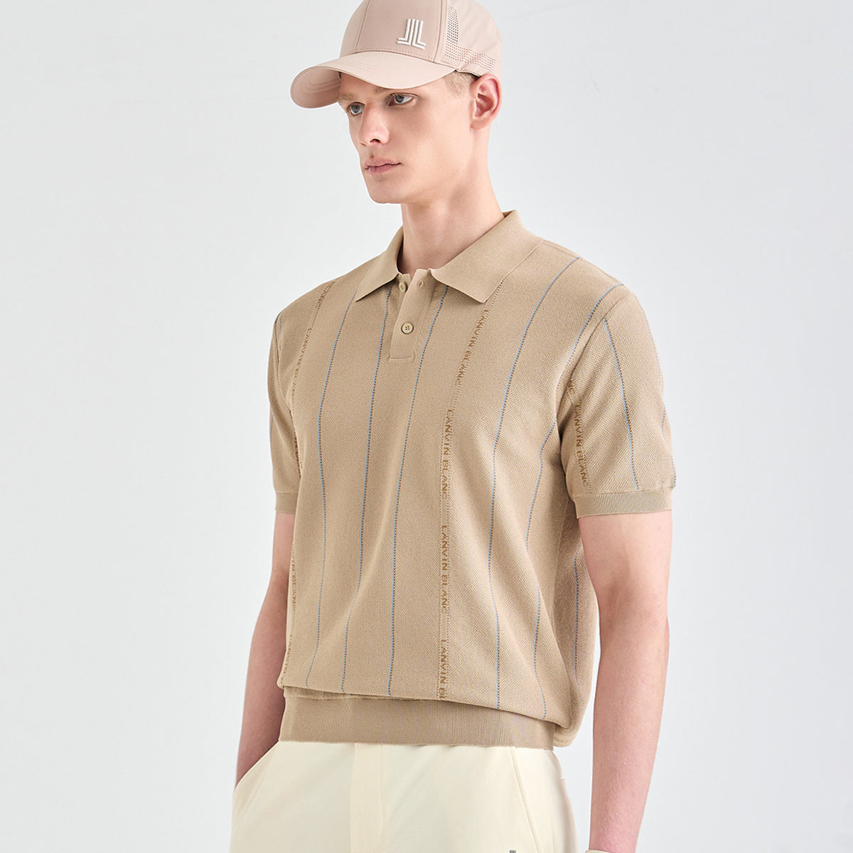 A man wearing a beige short-sleeve knit polo shirt with vertical blue stripes and a matching beige baseball cap, photographed against a clean light gray studio background.