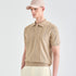 A man wearing a beige short-sleeve knit polo shirt with vertical blue stripes and a matching beige baseball cap, photographed against a clean light gray studio background.
