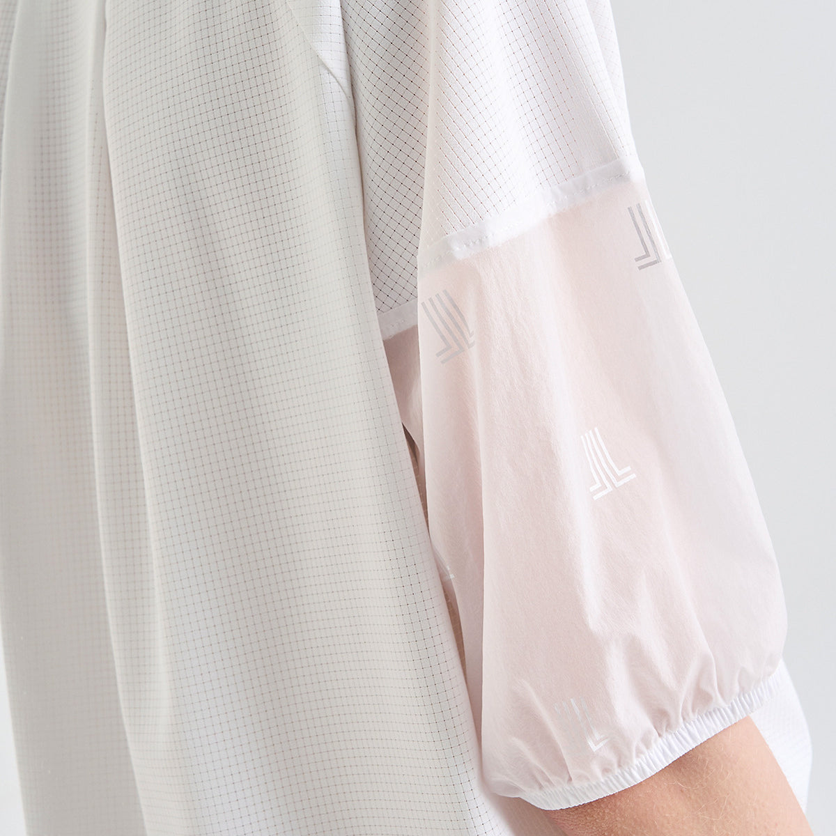 Close-up of a white sleeveless mesh top with sheer light pink puff sleeves featuring tonal embroidered geometric logos.