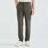 A person wearing slim-fit olive green trousers, styled with a cream and brown striped shirt and white sneakers, shown from the waist down on a light gray studio background.