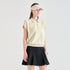 A woman modeling a light cream short-sleeve polo shirt with a black pleated tennis skirt and a beige visor, standing against a solid light gray background.