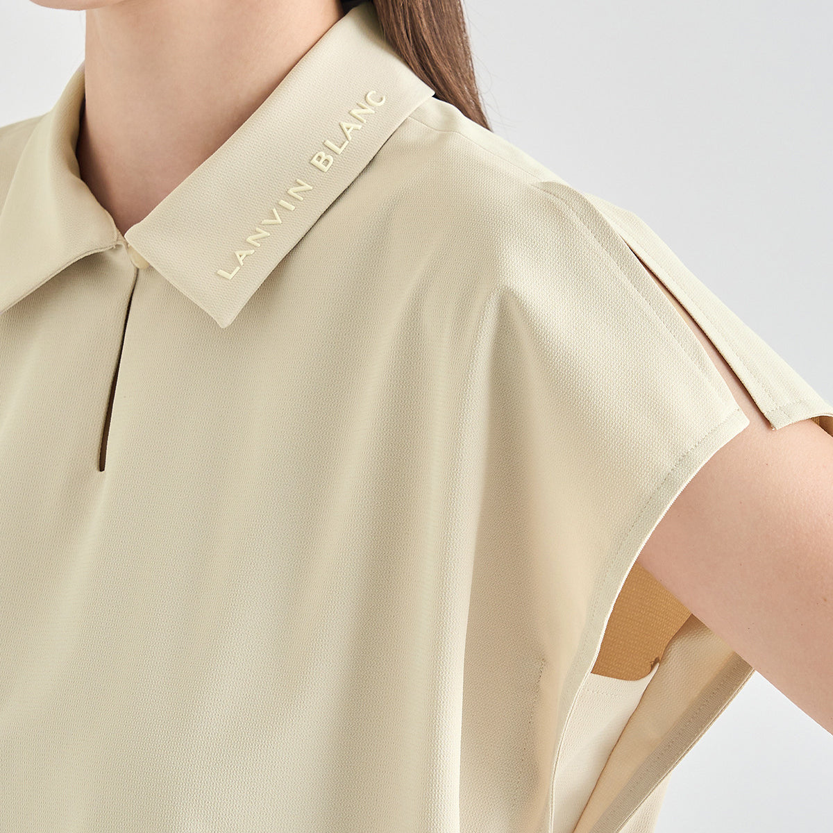Close-up of a model wearing a Lanvin Blanc short-sleeve polo shirt in a light beige color, showing the collar with the brand name embroidered on it.