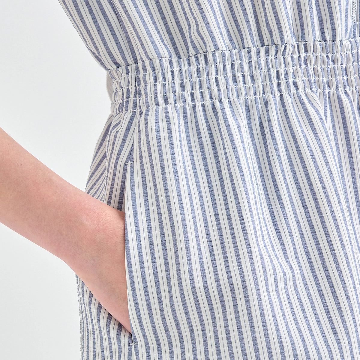 Close-up of a person wearing a smocked waist dress with vertical blue and white stripes, showing the side pocket and hand.