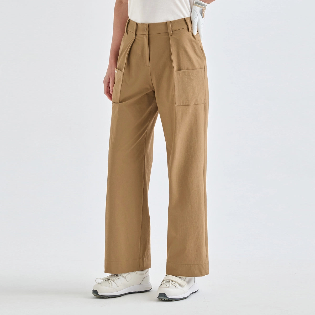 A person wearing tan wide-leg utility pants with a white top and white sneakers, shown from the waist down against a clean white studio background.