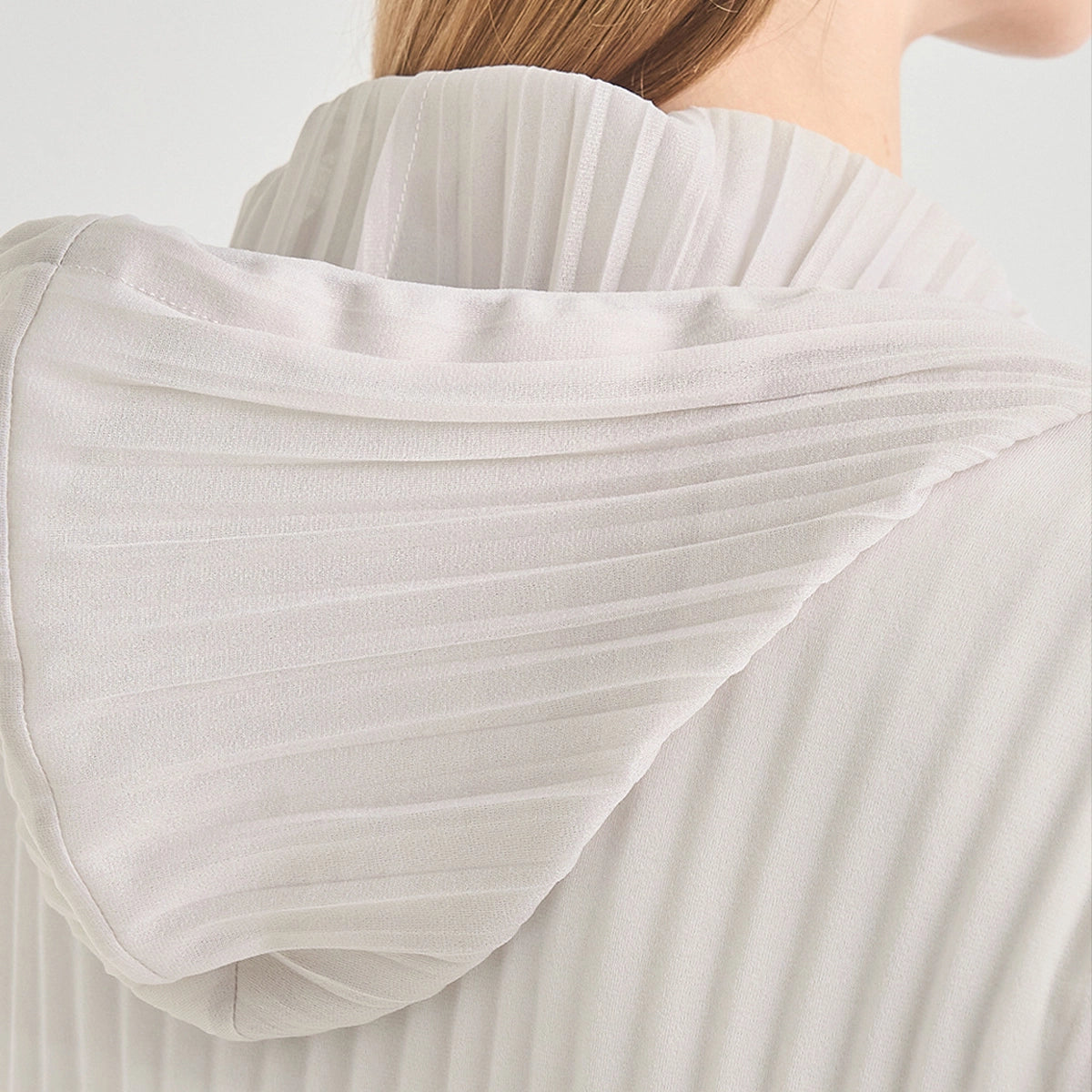 Close-up of a person wearing a white pleated top, showing the back of the neck and the high pleated collar with horizontal pleating details.
