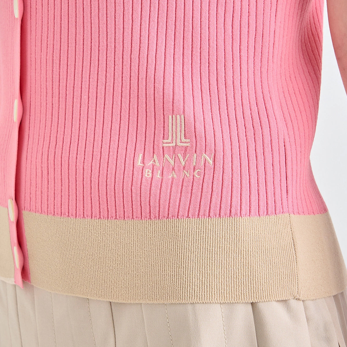 Close-up of a pink ribbed knit cardigan with a beige band and gold-toned 'LANVIN BLANC' logo on the chest, worn over a light beige skirt.