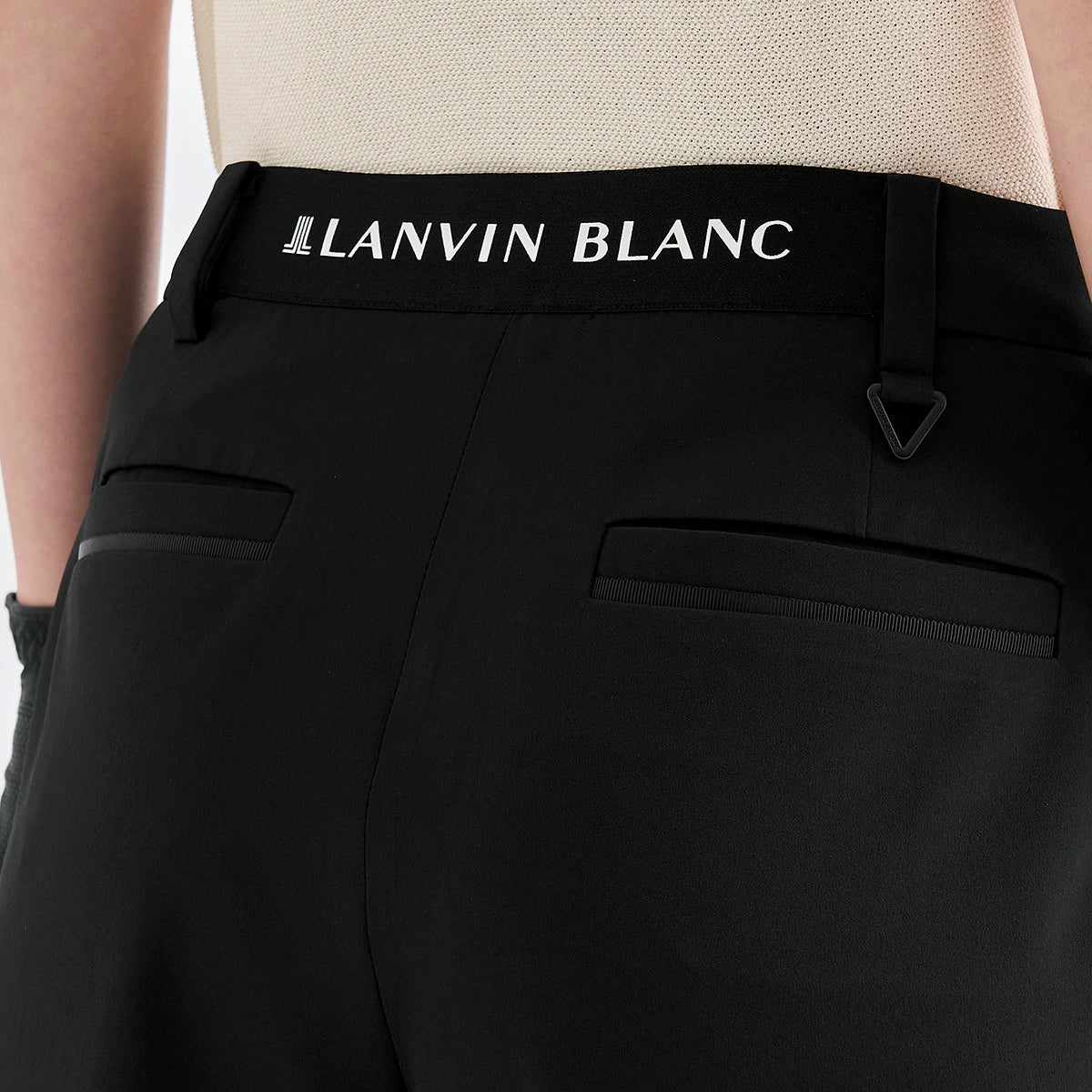 Close-up of the back waistband of black Lanvin Blanc trousers, featuring a black elastic waistband with white brand lettering and a small triangular metal hook detail.