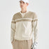 A man wearing a beige and off-white color-blocked zip-up golf jacket, beige pants, a white cap, and a white golf glove, photographed against a clean light gray studio background.