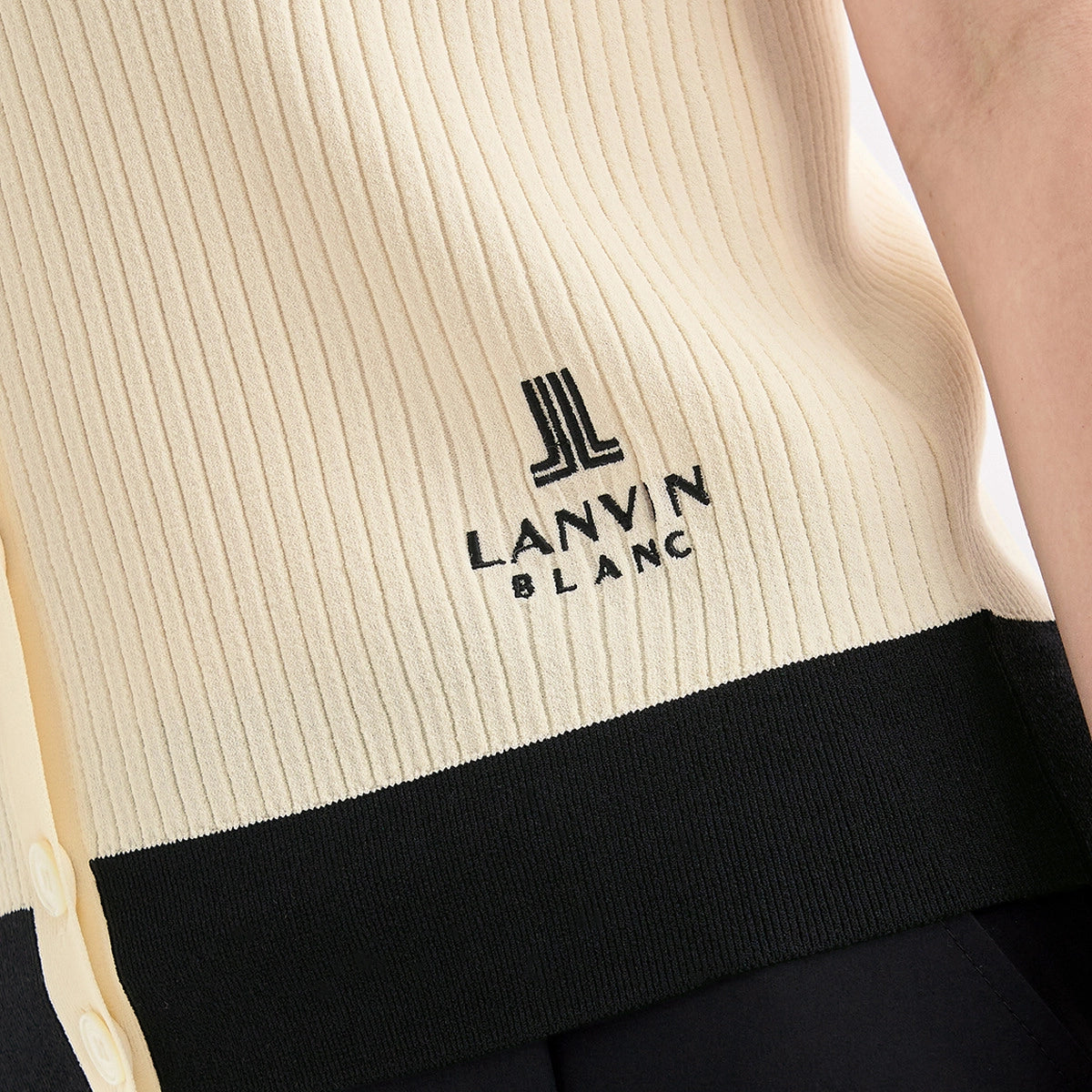 Close-up of a ribbed knit sweater in cream and black, featuring the black embroidered Lanvin Blanc logo on the chest.