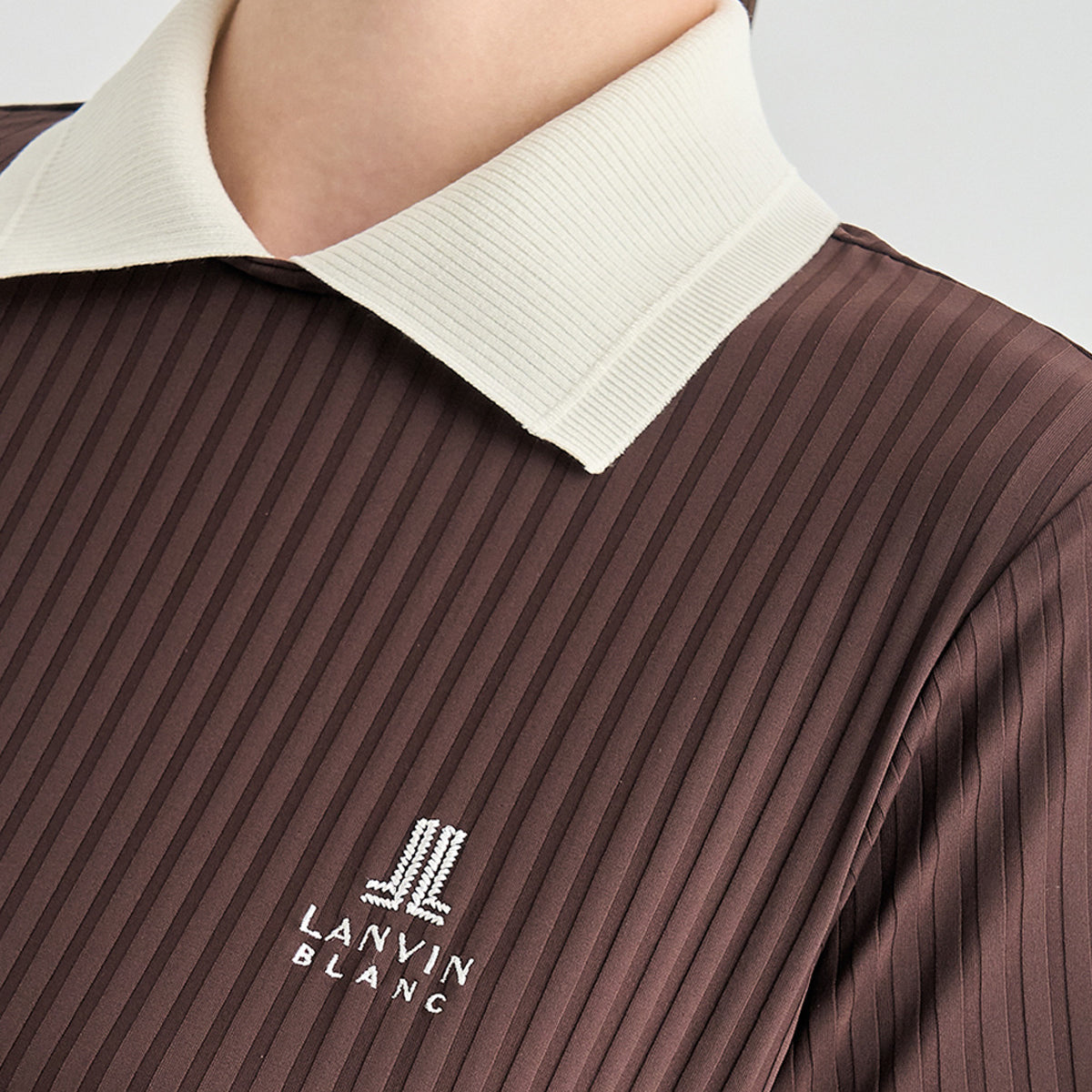 Close-up of a person wearing a brown ribbed collared top with a cream collar and a white LANVIN BLANC logo on the chest.