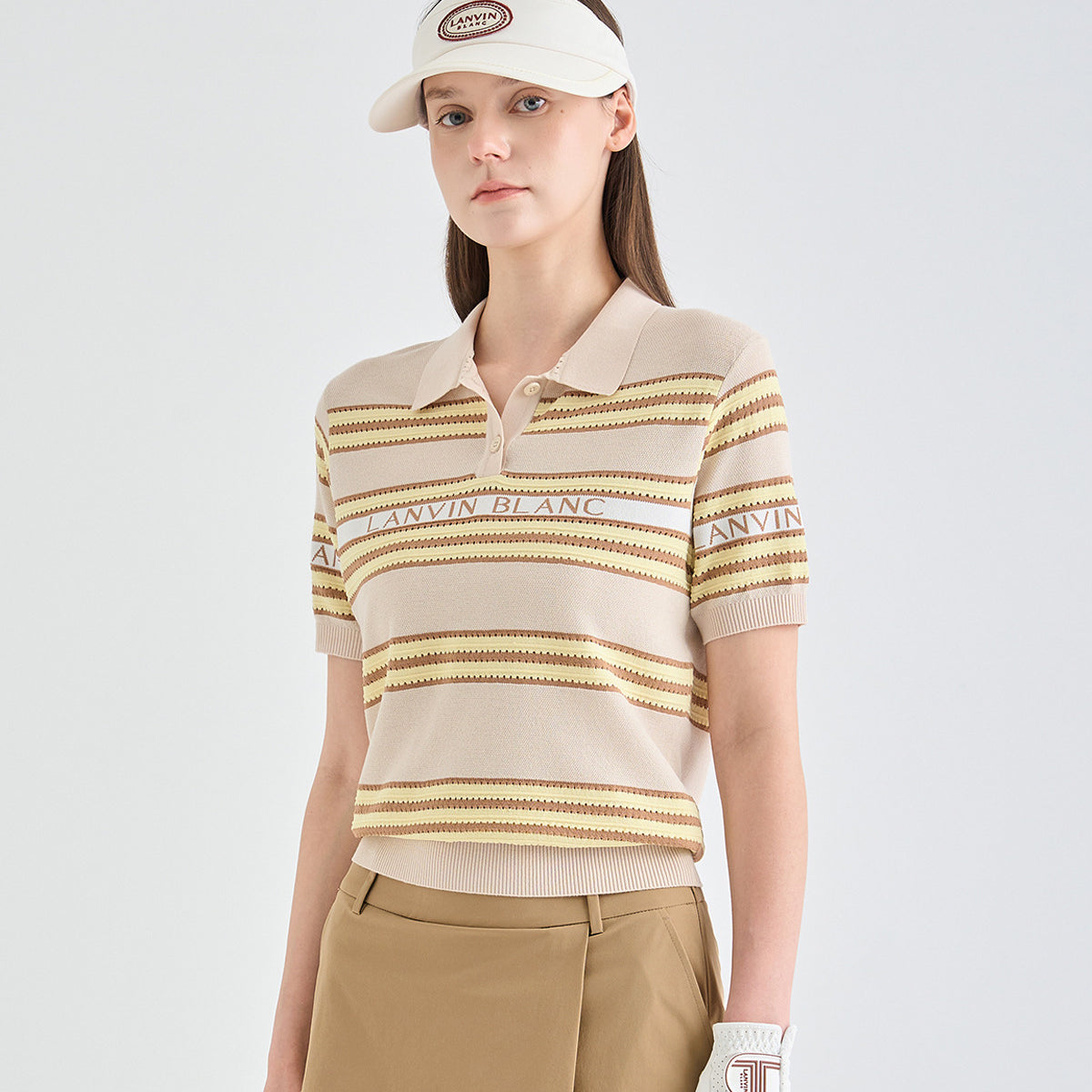 A model wearing a beige and brown striped knit polo shirt with 'LANVIN BLANC' text across the chest, paired with khaki pants and a white visor.