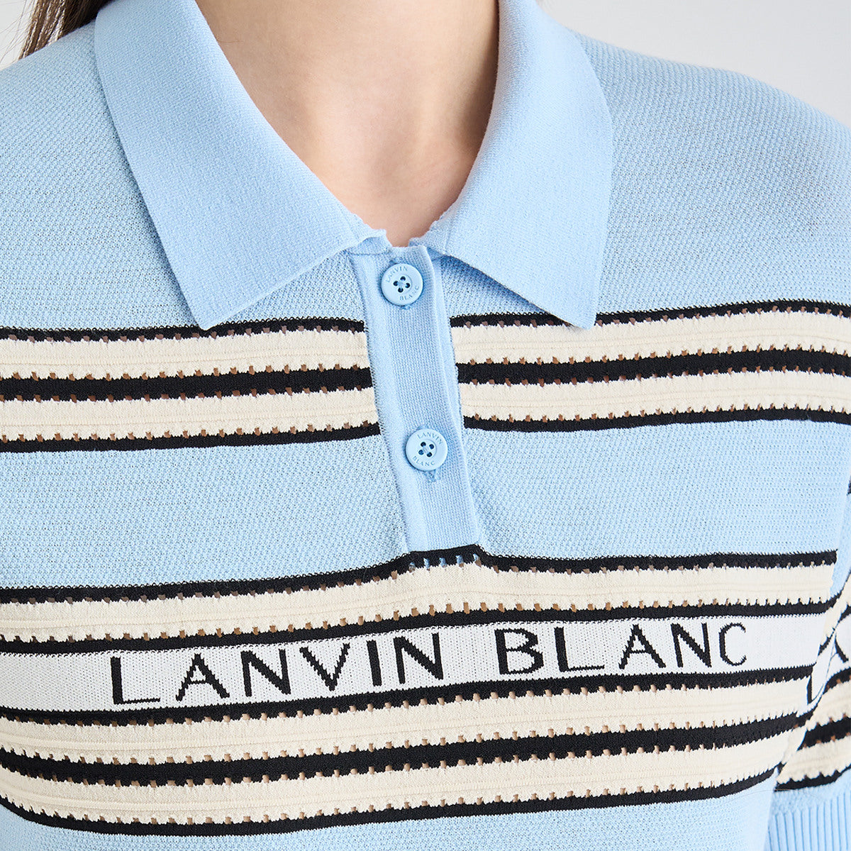 Close-up of a light blue knit polo shirt with black and cream horizontal stripes and the text 'LANVIN BLANC' across the chest, worn by a model.