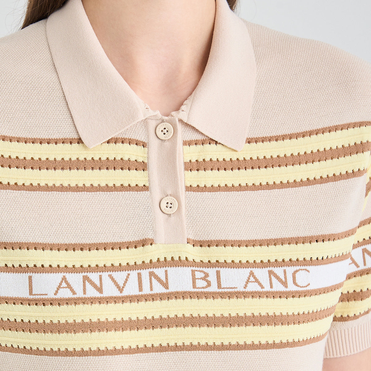 Close-up of a knit polo shirt with horizontal beige, cream, and brown stripes, featuring a white stripe with 'LANVIN BLANC' text across the chest and a two-button placket.