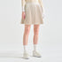 A model wearing a pleated beige mini skirt, cream knit long-sleeve top, white gloves, white socks, and cream platform sneakers, shown from the waist down against a light gray studio background.