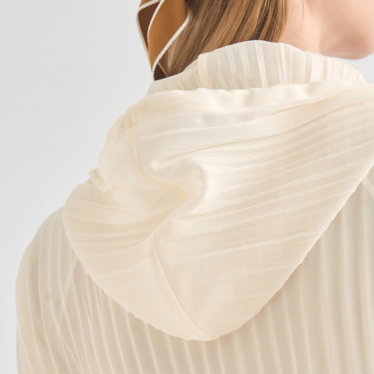Close-up of a person wearing a cream-colored pleated top, showing the back of the neck and the textured fabric of the garment.