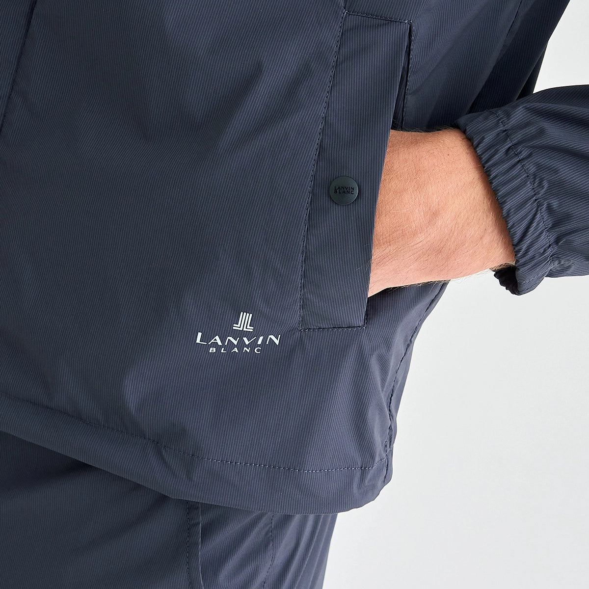 Close-up of a navy lightweight jacket with a side pocket, showing a hand in the pocket and the white LANVIN BLANC logo near the hem.
