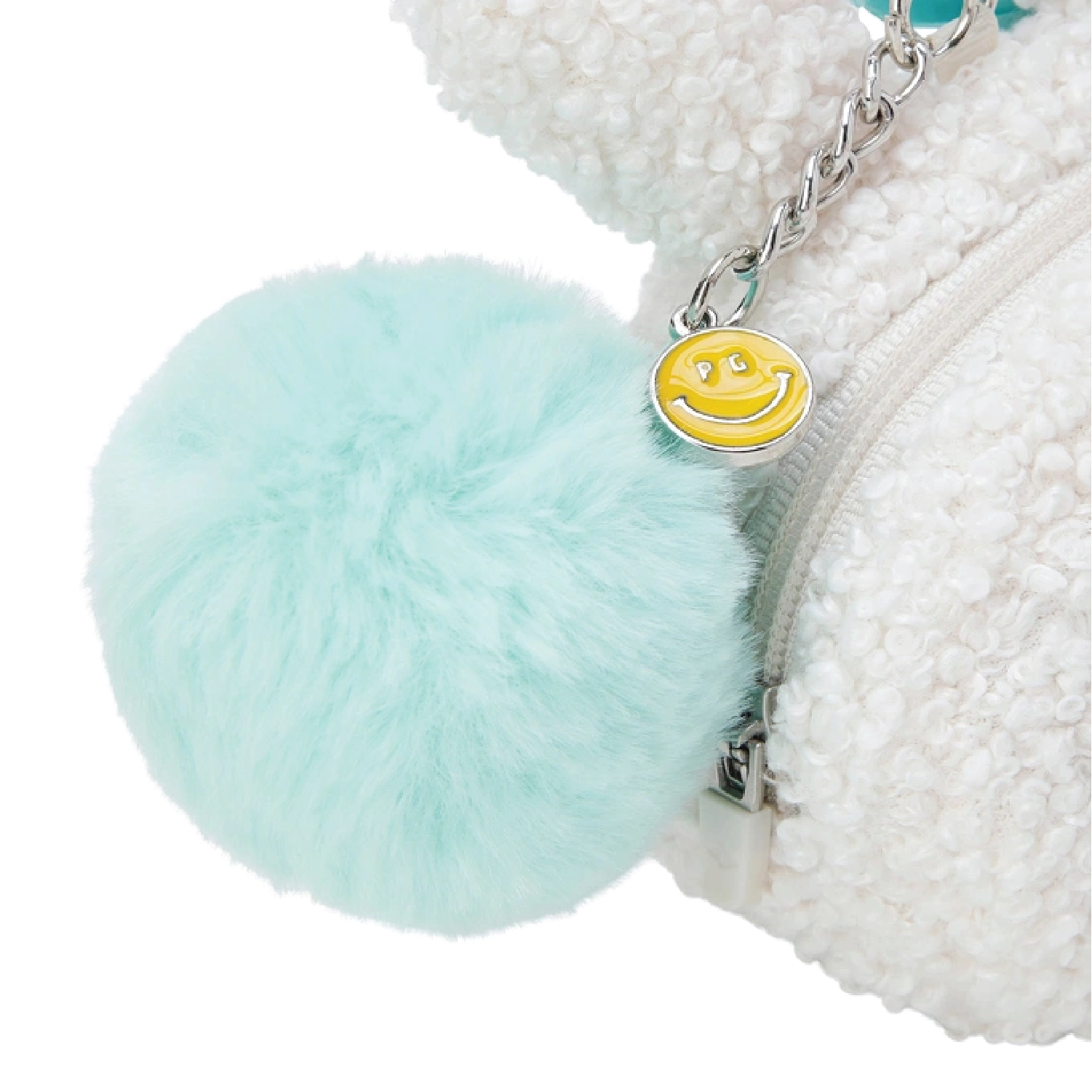 A close-up of a white sherpa fleece zippered pouch featuring a large mint green faux fur pom-pom and a silver chain with a yellow smiley face charm.