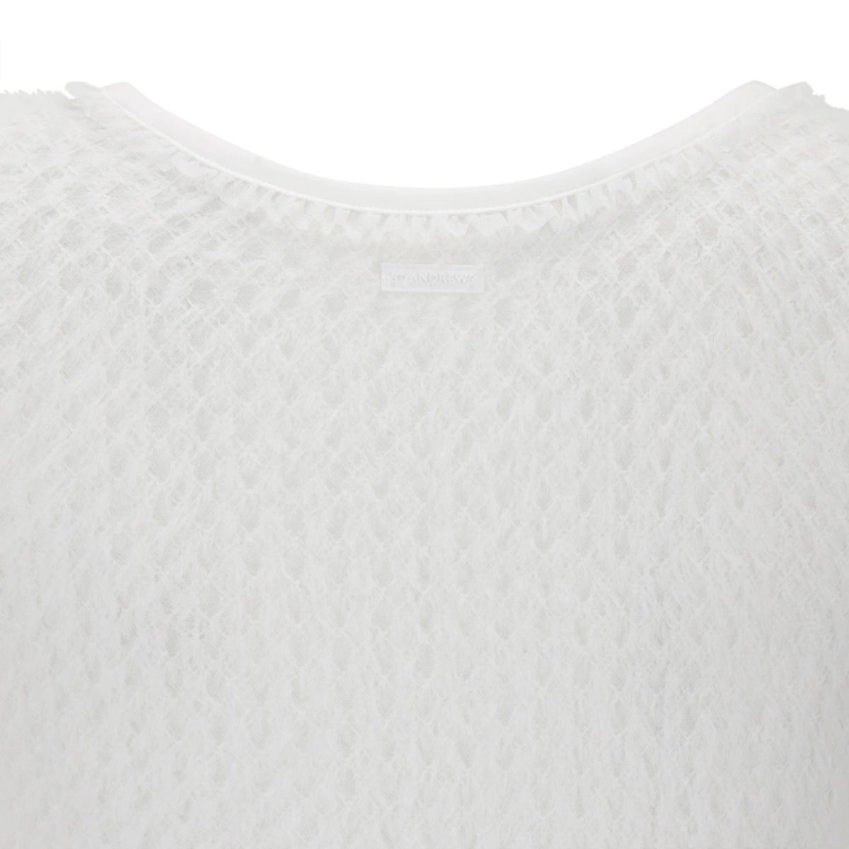 Close-up of a white textured knit top showing the crew neckline and a small interior brand label.