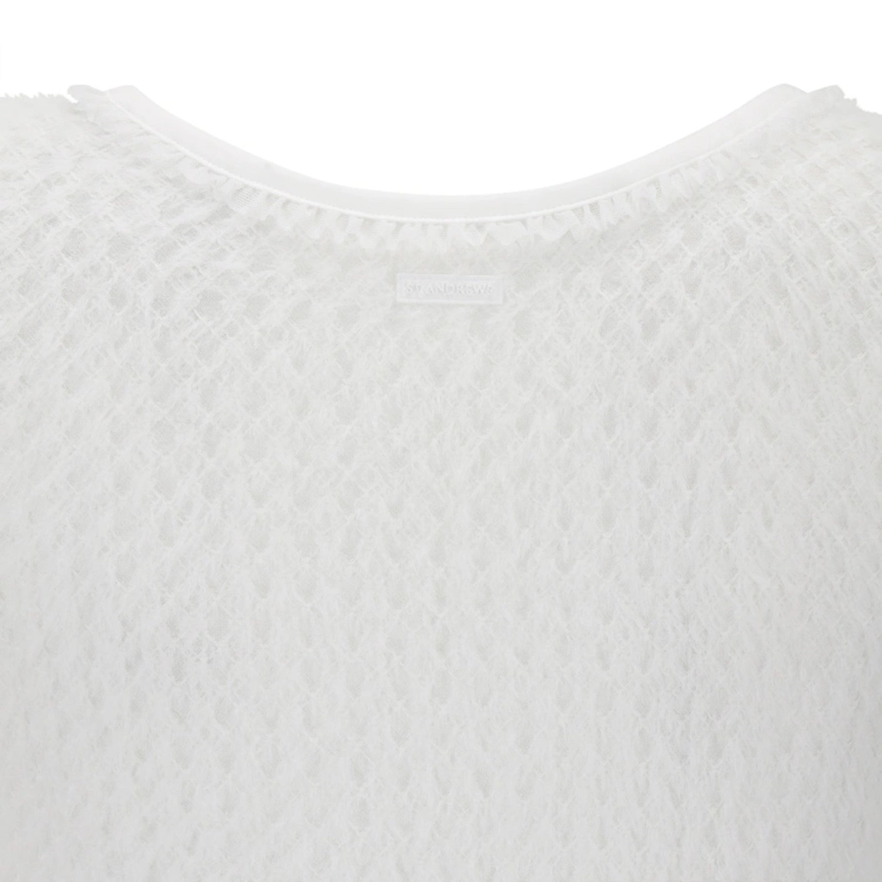Close-up of a white textured knit top showing the crew neckline and a small interior brand label.