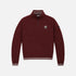 A maroon long-sleeve quarter-zip pullover sweatshirt with white striped ribbing on the collar, cuffs, and hem, featuring a small embroidered shield logo on the left chest.